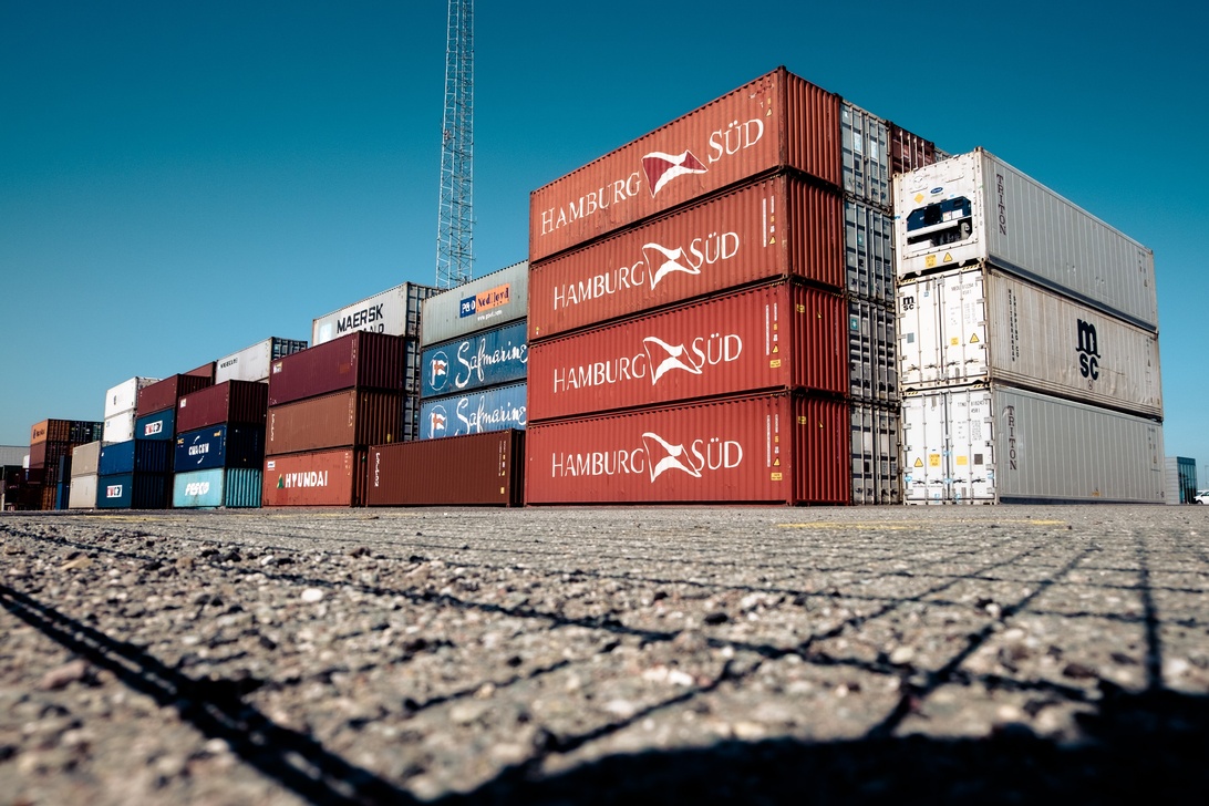 Fargerike shippingcontainere stablet i en havn, illustrerer logistikken og de mange leddene i bilimport.
