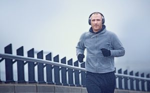 Middle aged man jogging in the city in winter listening to music on his wireless headphones